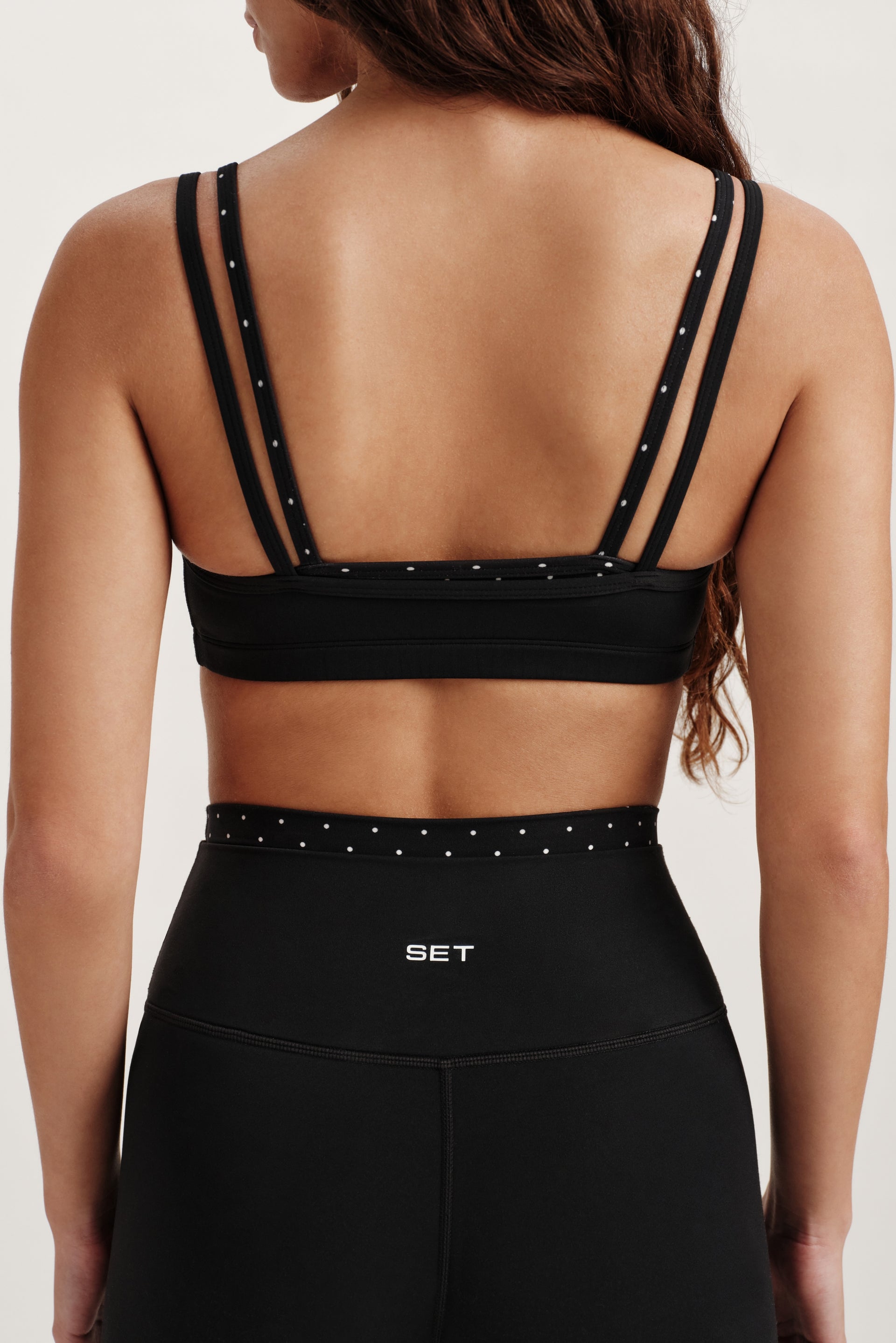Black sports bra with thin straps and studded details on a neutral background