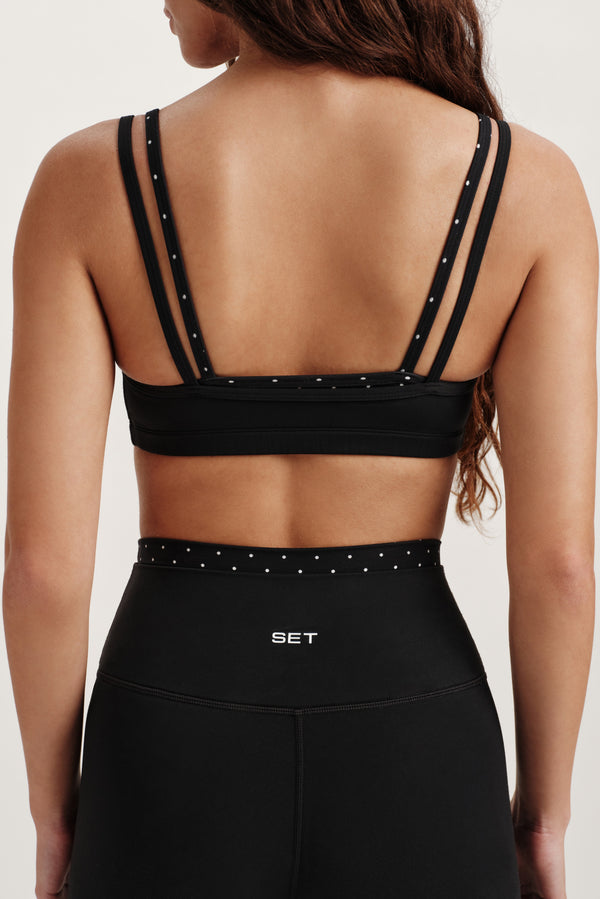 Black sports bra with thin straps and studded details on a neutral background