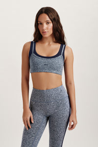 Woman wearing a gray sports bra and leggings set on a plain background 