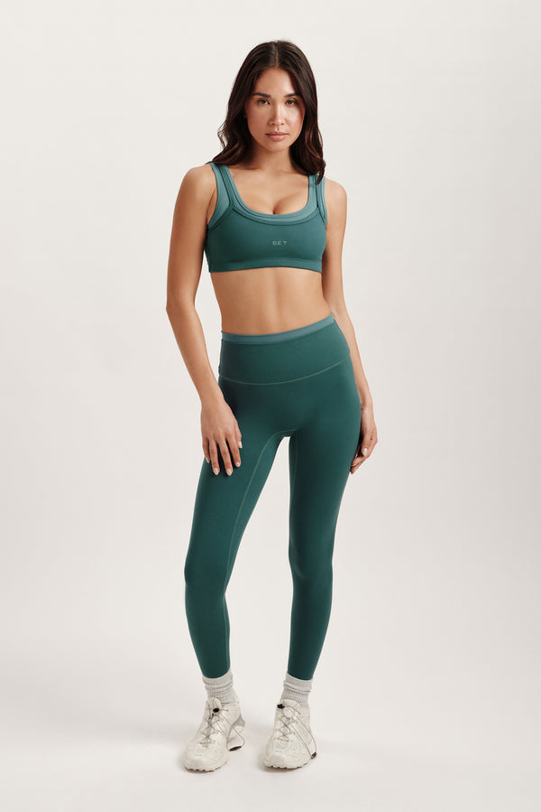 Woman wearing a green sports bra and leggings set on a white background