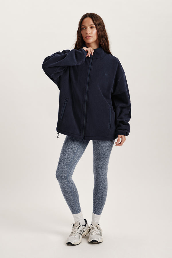 Person wearing a navy jacket and gray leggings on a white background