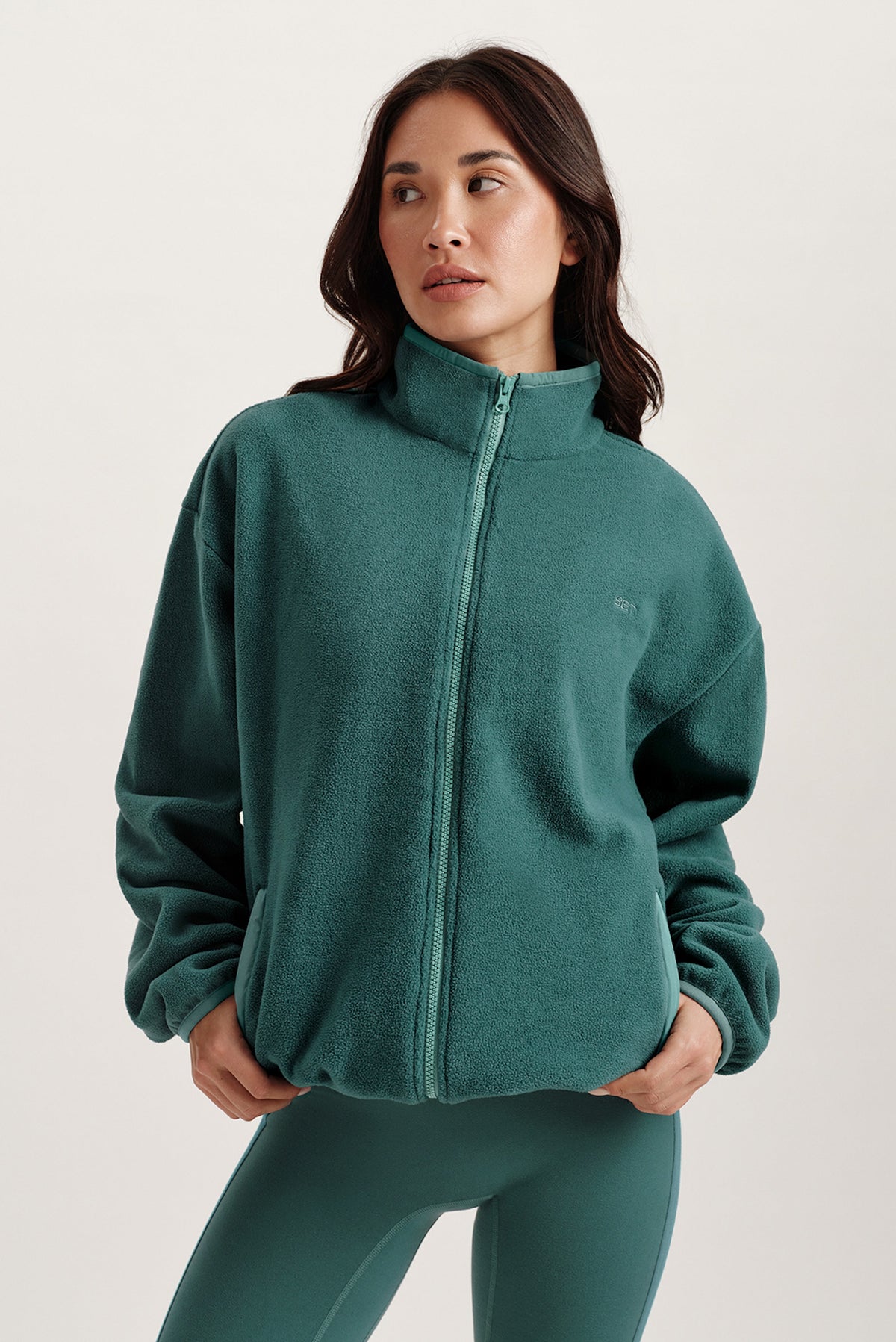 Woman wearing a teal fleece jacket and leggings on a light background 
