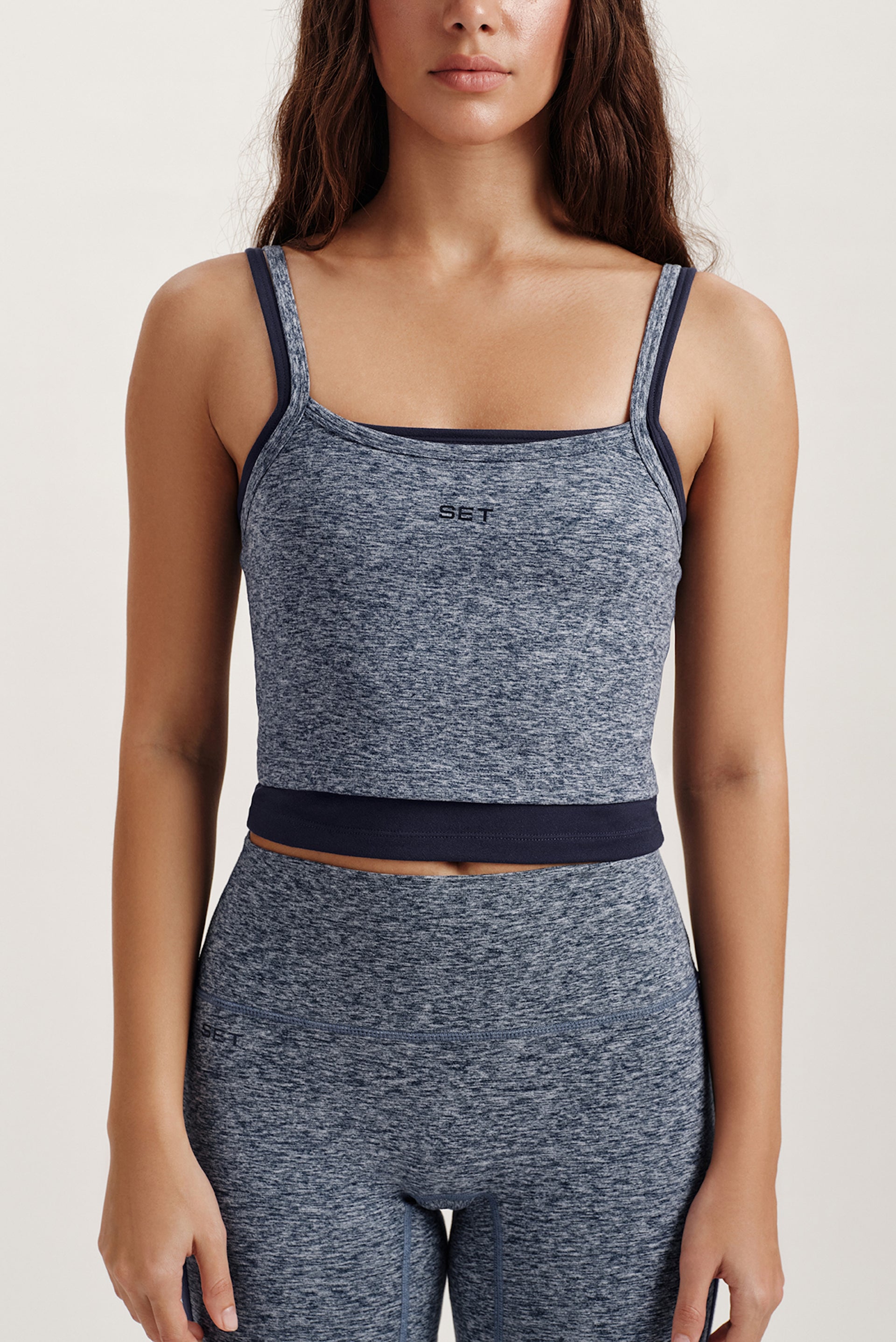 Woman wearing a gray sports bra and leggings set on a white background