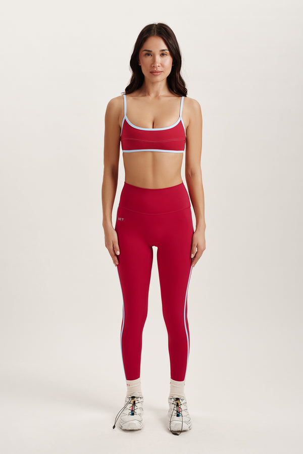 Woman wearing a red athletic outfit with a white sports bra and leggings on a light gray background