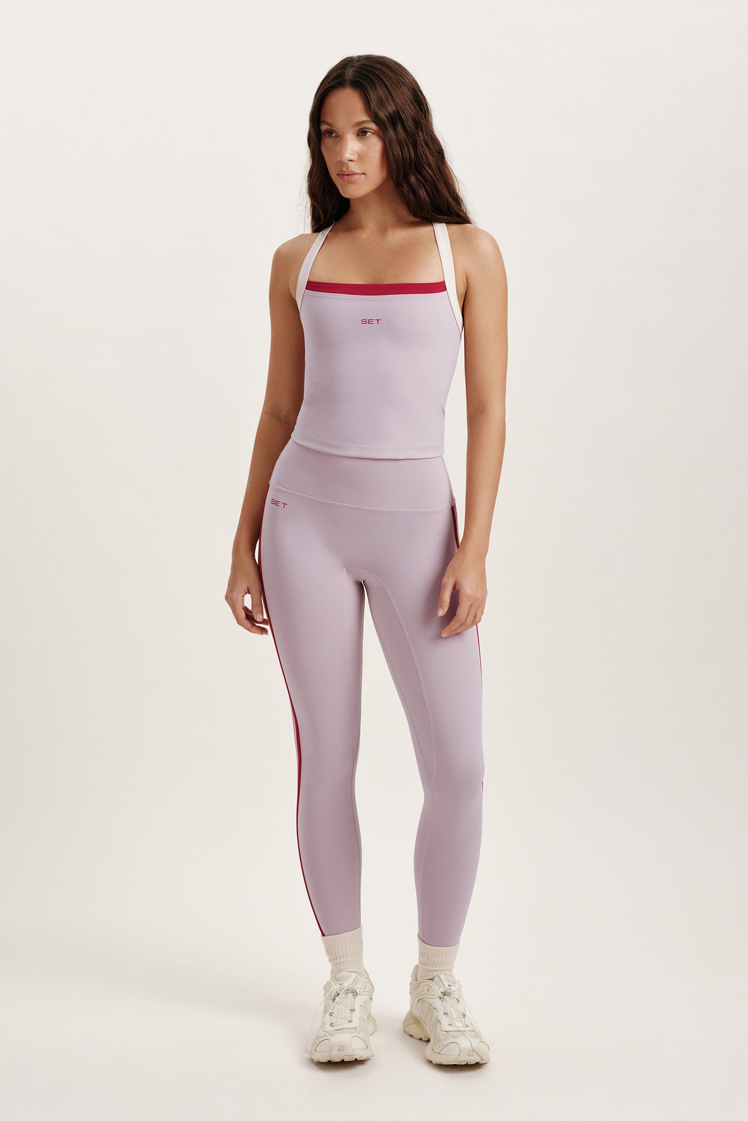 Woman wearing a light purple active set with red accents on a white background