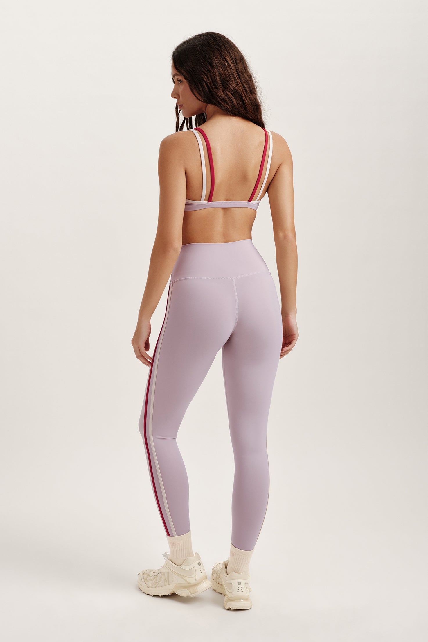 Woman wearing a light purple athletic outfit with red stripes on a white background