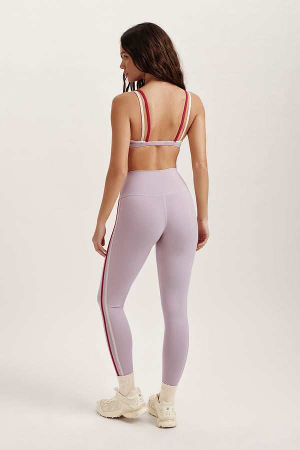 Woman wearing a light purple athletic outfit with red stripes on a white background