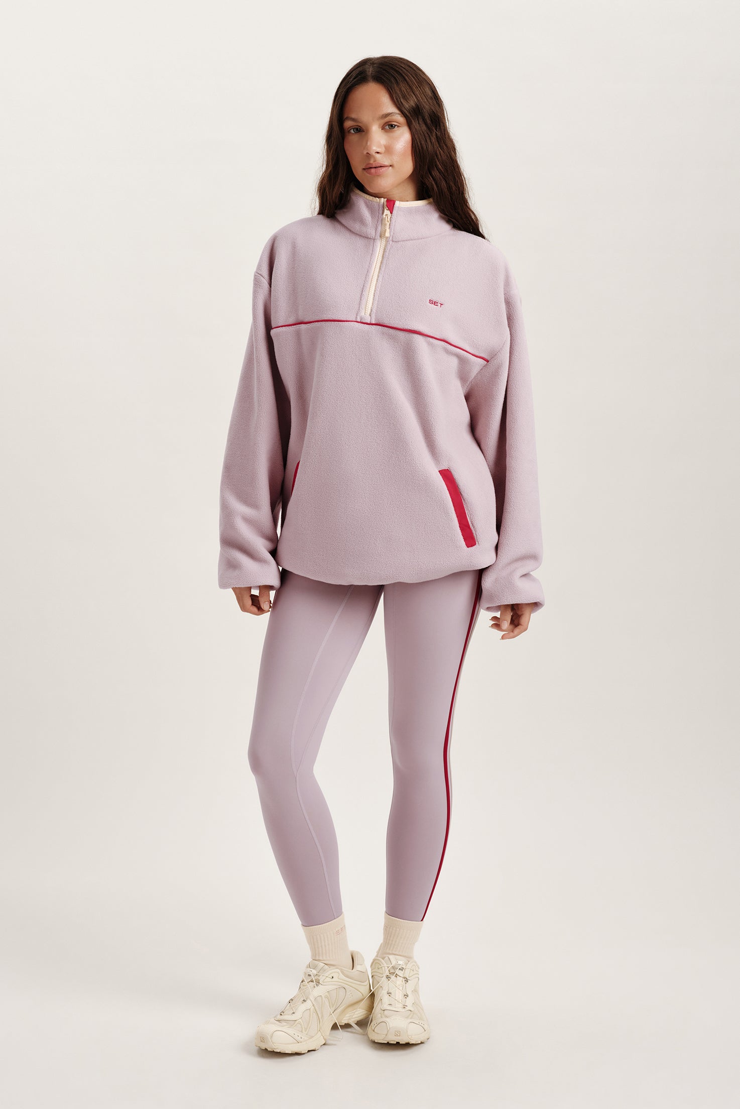 Woman wearing a light purple tracksuit with red accents on a white background