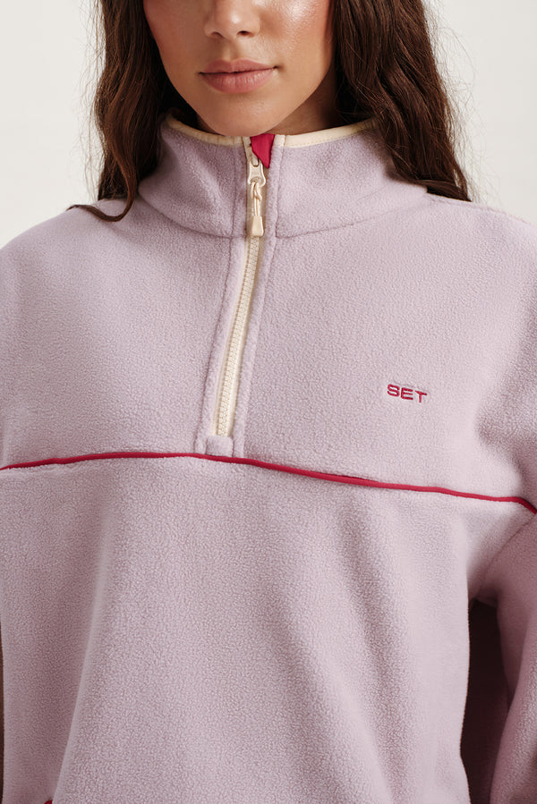 Close-up of a person wearing a light purple fleece jacket with a zipper, featuring the brand 'SET'.
