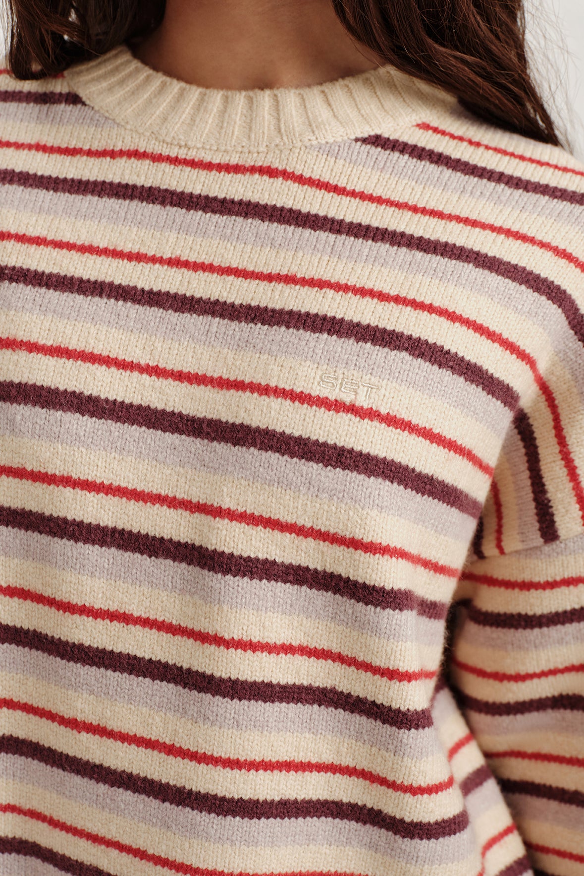 Close-up of a person wearing a striped sweater with red, brown, and beige colors.