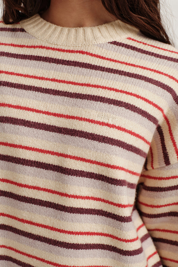 Close-up of a person wearing a striped sweater with red, brown, and beige colors.