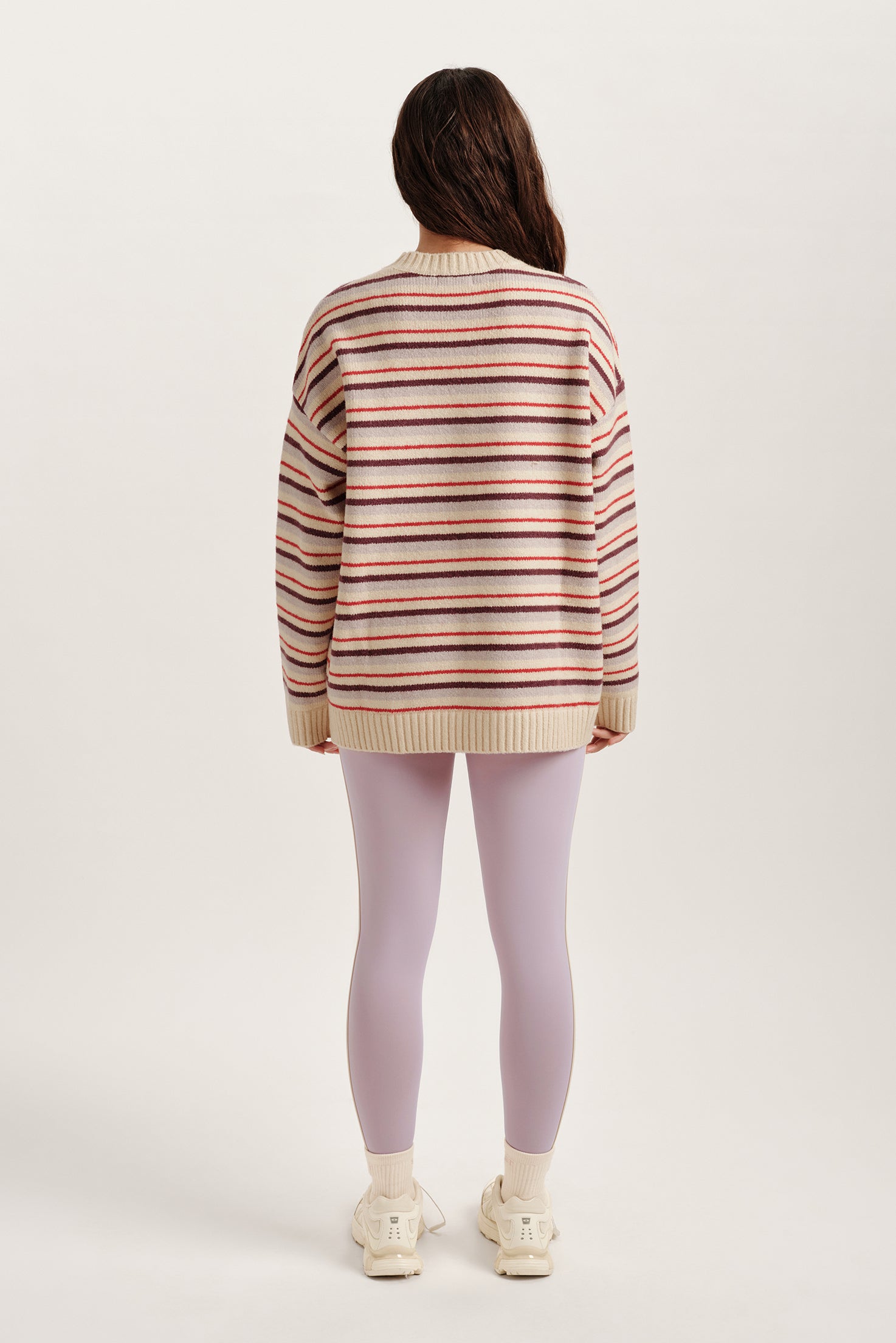 Person wearing a striped sweater and light purple leggings on a white background