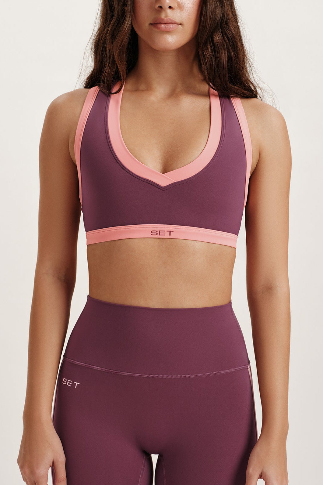 Woman wearing a maroon sports bra and leggings with pink accents on a white background