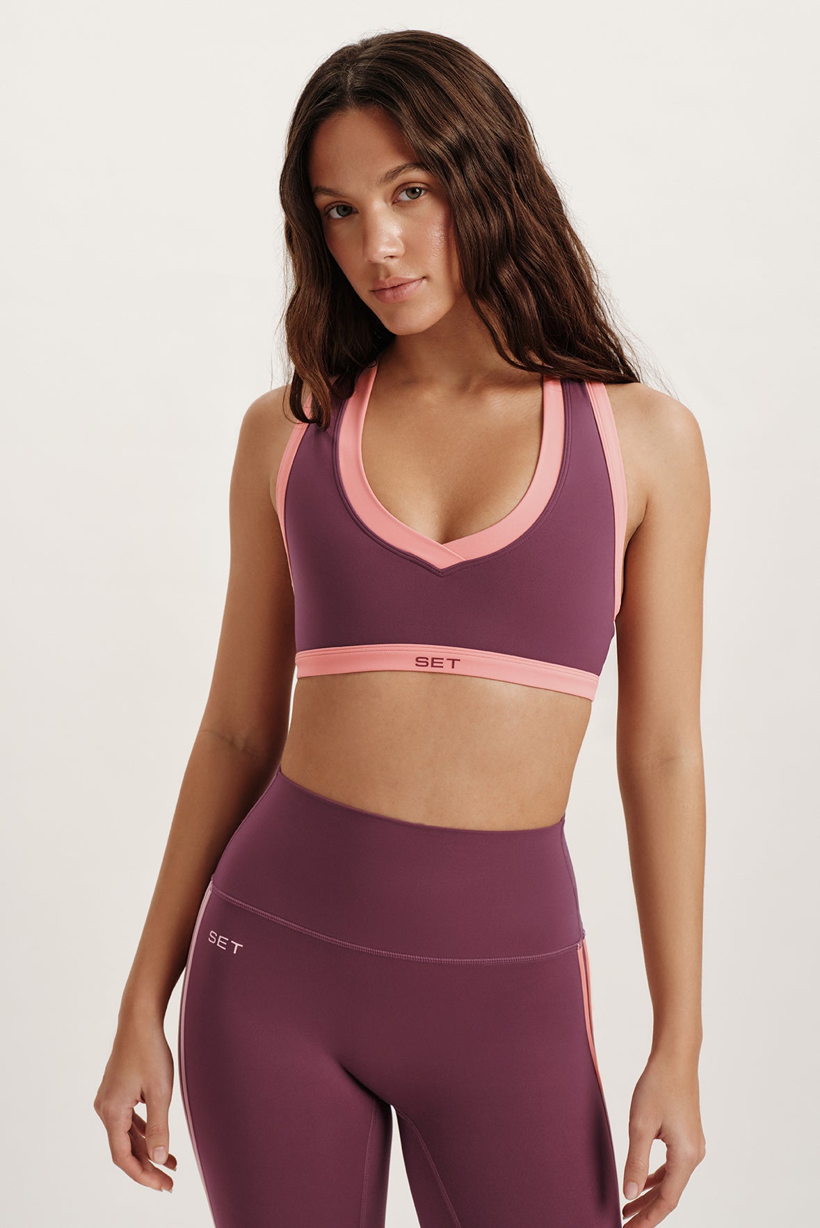 Woman wearing a purple sports bra and leggings with pink accents on a white background 