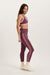Woman wearing a purple sports bra and leggings with white stripes on a white background