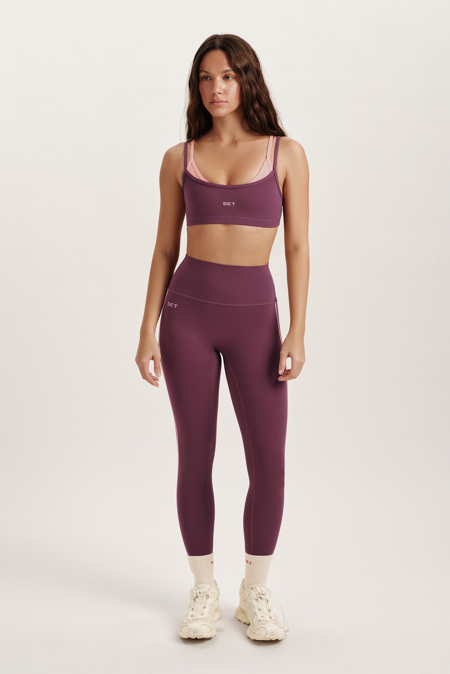 Woman wearing a purple sports bra and leggings set on a white background