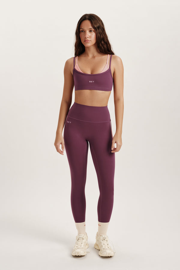 Woman wearing a purple sports bra and leggings set on a white background