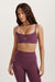 Woman wearing a purple sports bra and leggings set on a light background <model-info>Brinley wears a size XS and is 5’8, 23” waist, 32A bust.</model-info> 