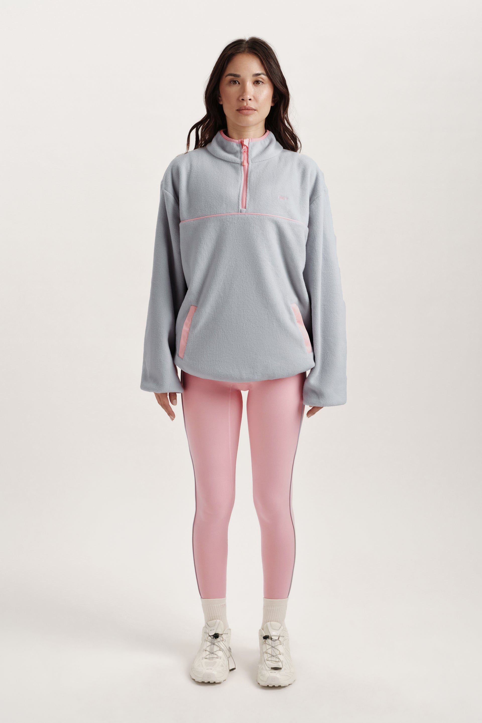 Woman wearing a blue fleece pullover with pink accents and pink leggings on a white background