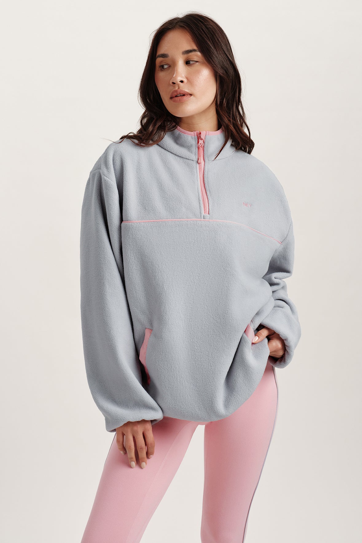 Woman wearing a blue pullover with pink accents on a light background