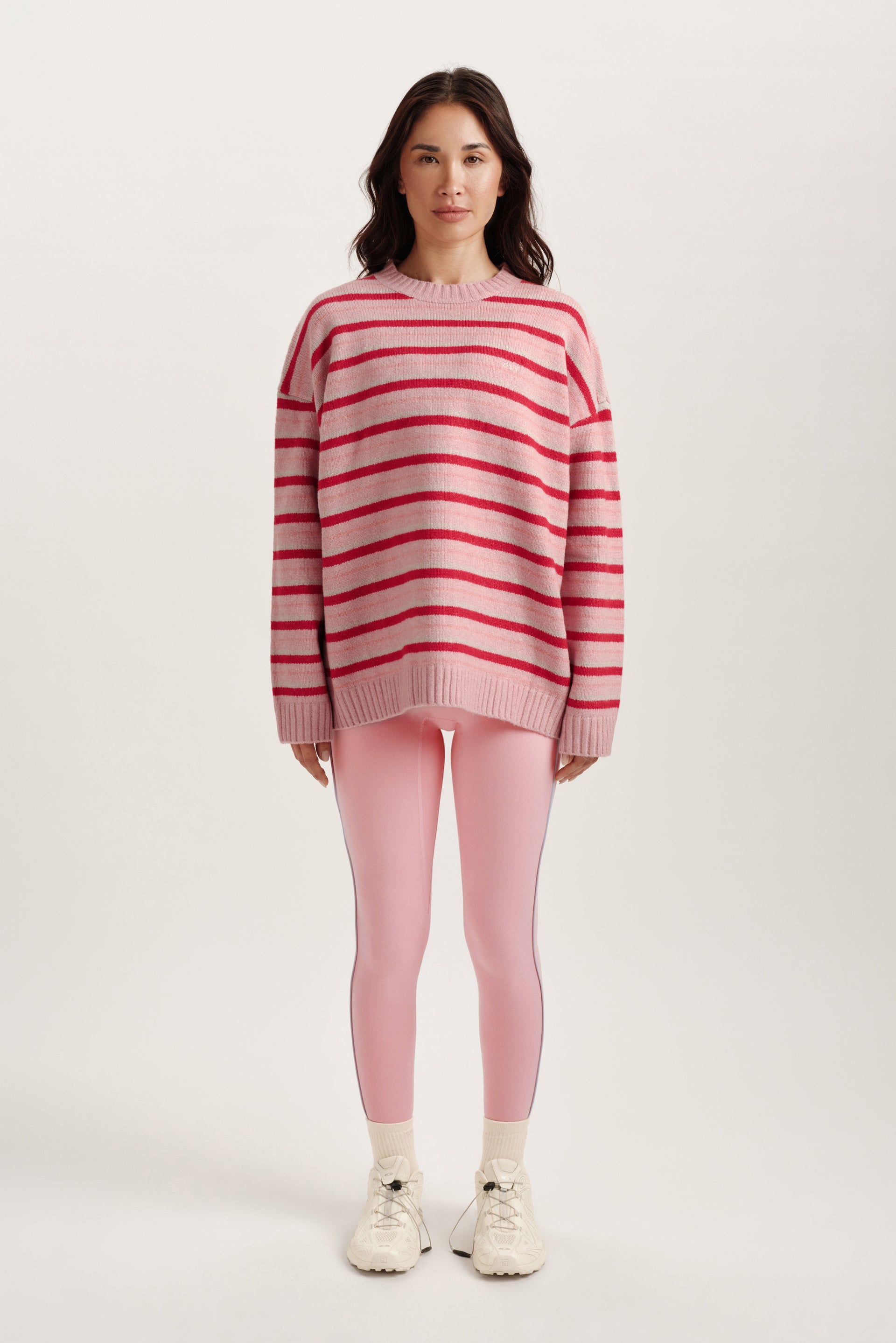 Woman wearing a pink and red striped sweater and pink leggings on a white background