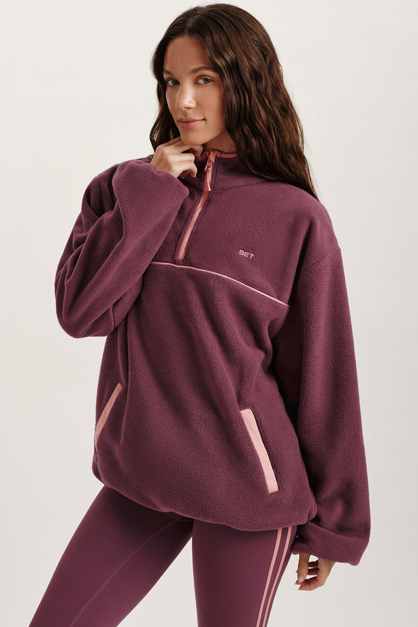 Woman wearing a maroon fleece pullover with a small logo on a white background