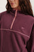 Close-up of a person wearing a maroon fleece pullover with a brand logo on a white background