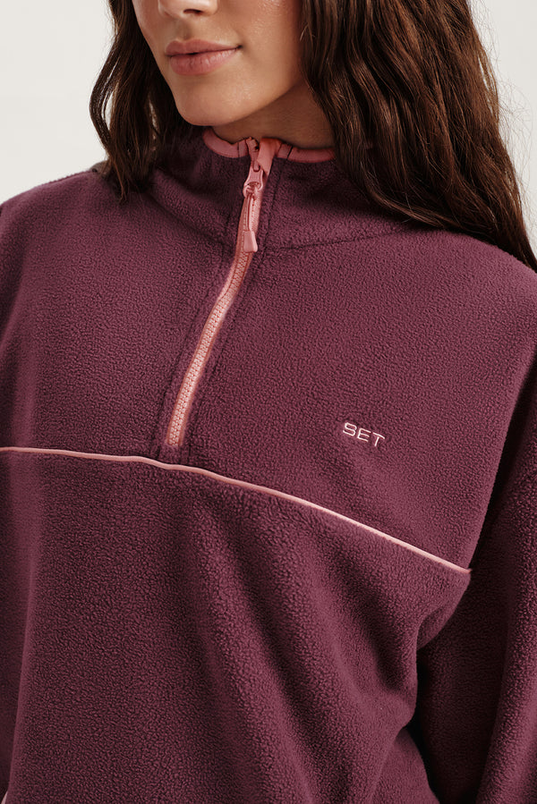 Close-up of a person wearing a maroon fleece pullover with a brand logo on a white background