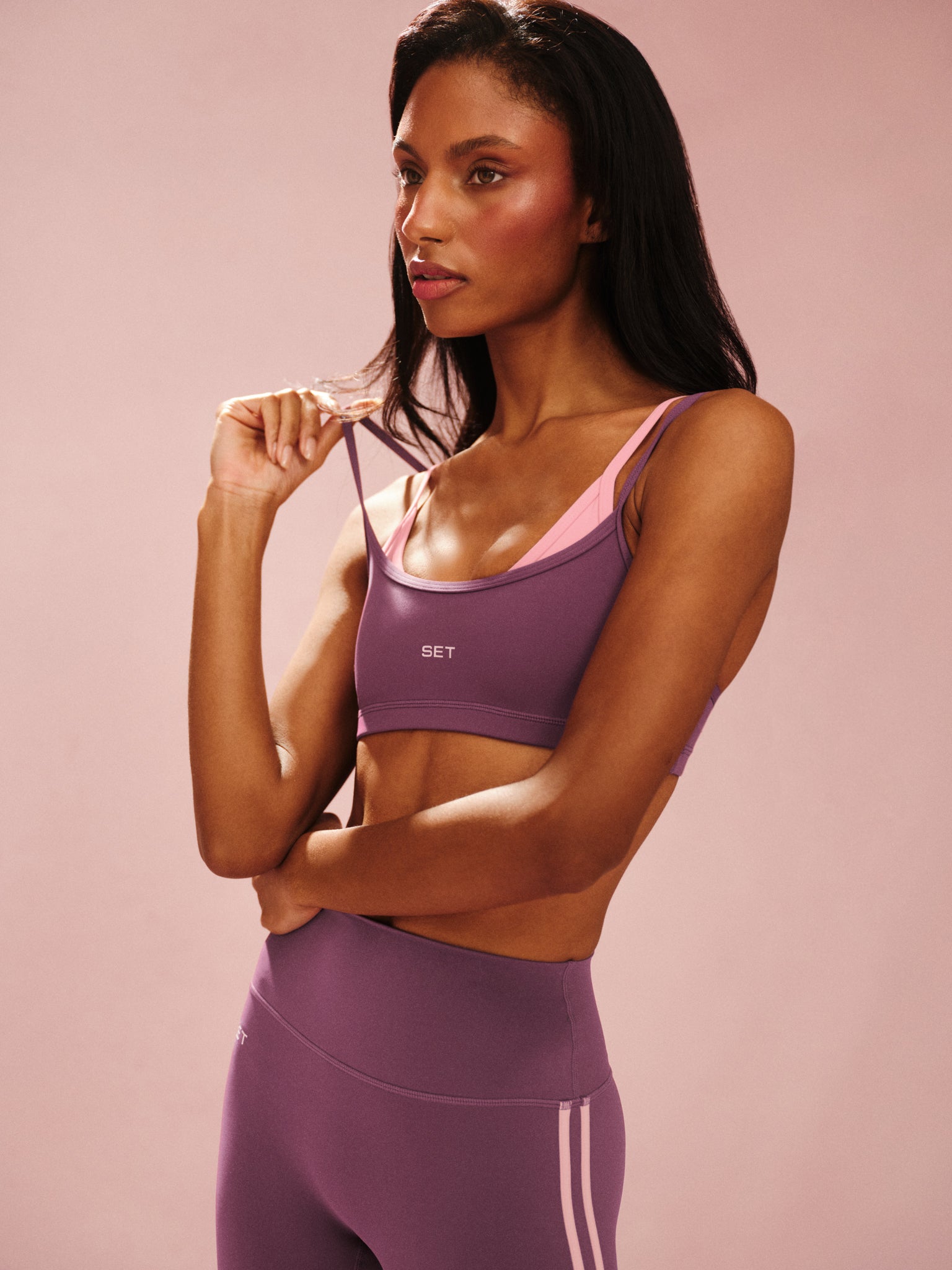 Woman wearing a purple sports bra and leggings with a pink background