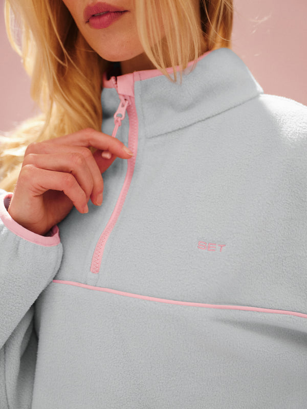 Blue fleece jacket with pink zipper and trim on a pink background