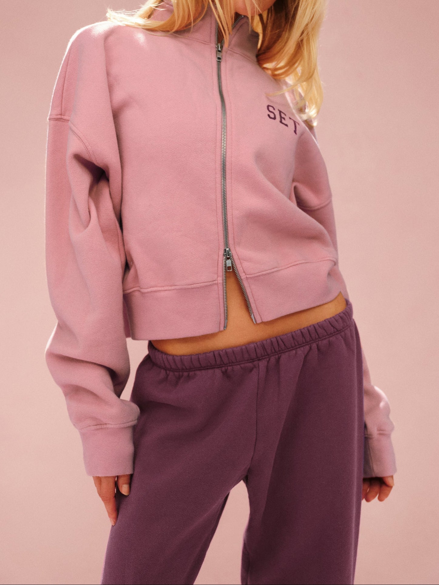 Person wearing a pink tracksuit with 'SET' branding on a pink background