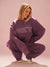 Person wearing a purple 'SET' sweatshirt and pants on a pink background