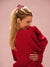 Woman wearing a red sweater against a pink background with a red claw clip in hair