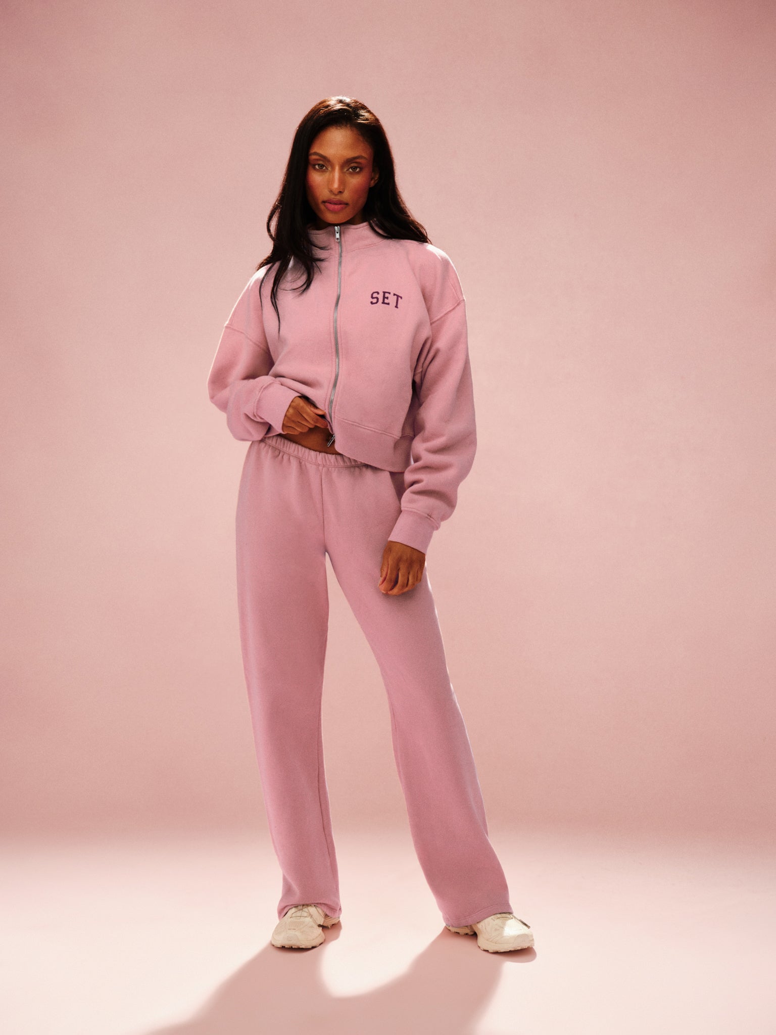 Woman wearing a pink tracksuit with 'SET' branding on a pink background