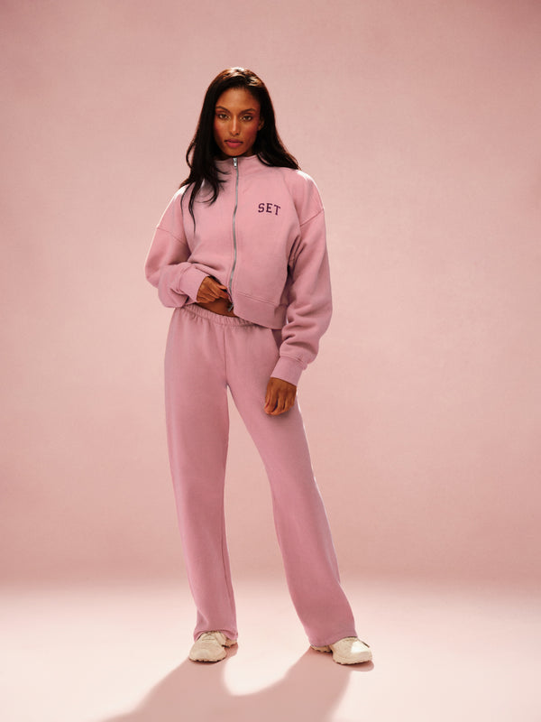 Woman wearing a pink tracksuit with 'SET' branding on a pink background