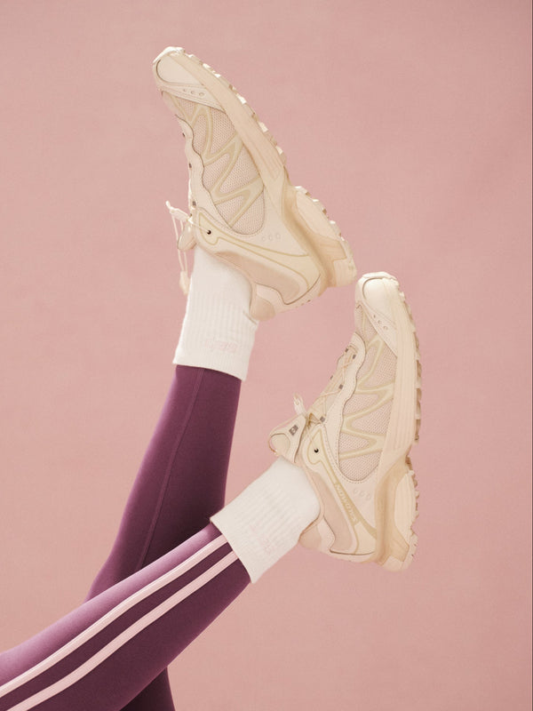 Beige sneakers, purple leggings with pink stripes and white crew socks on a pink background