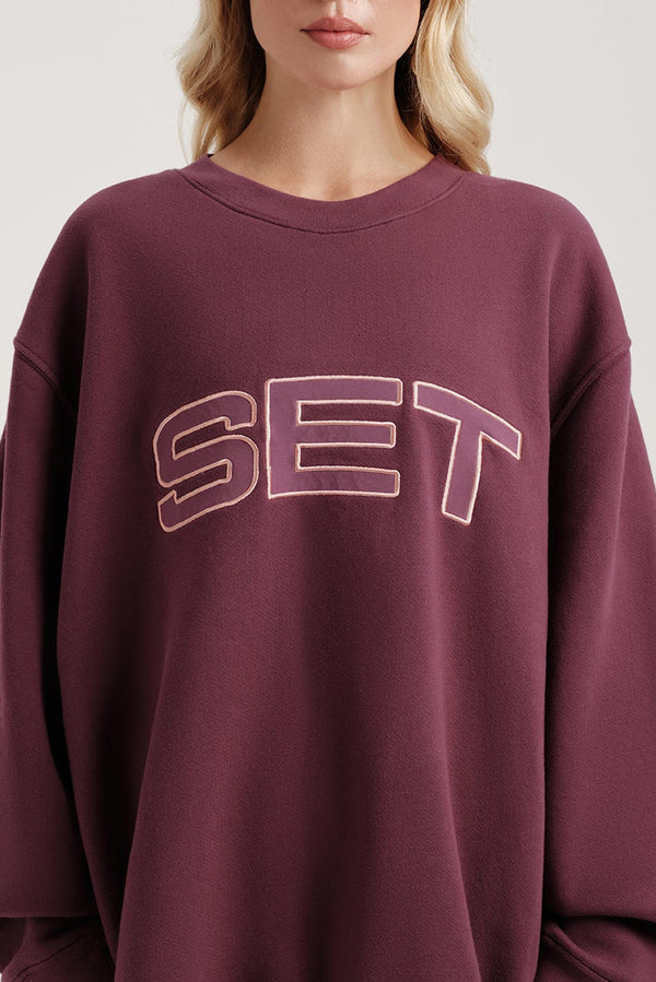 Maroon sweatshirt with 'SET' text worn by a person on a light background