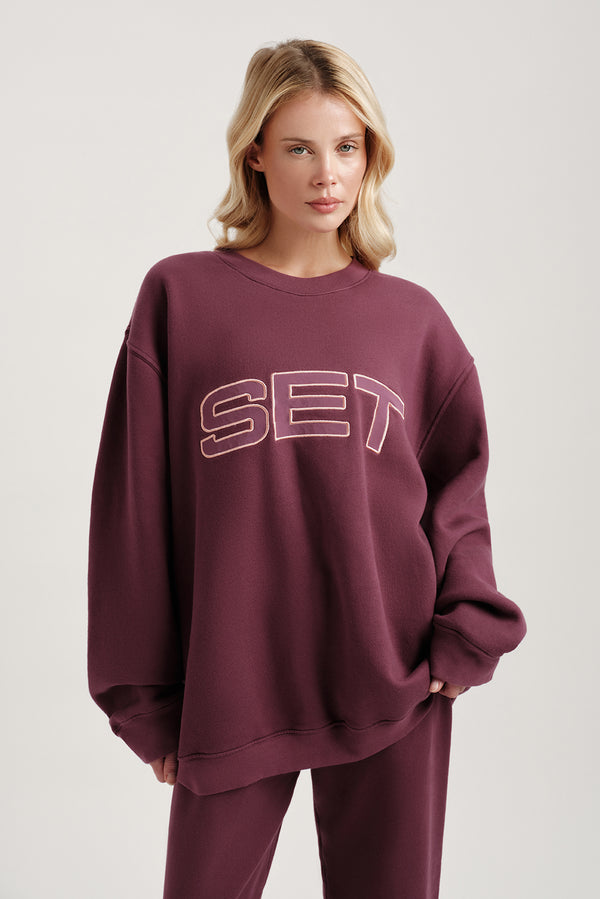 Woman wearing a maroon sweatshirt with 'SET' text on a plain background