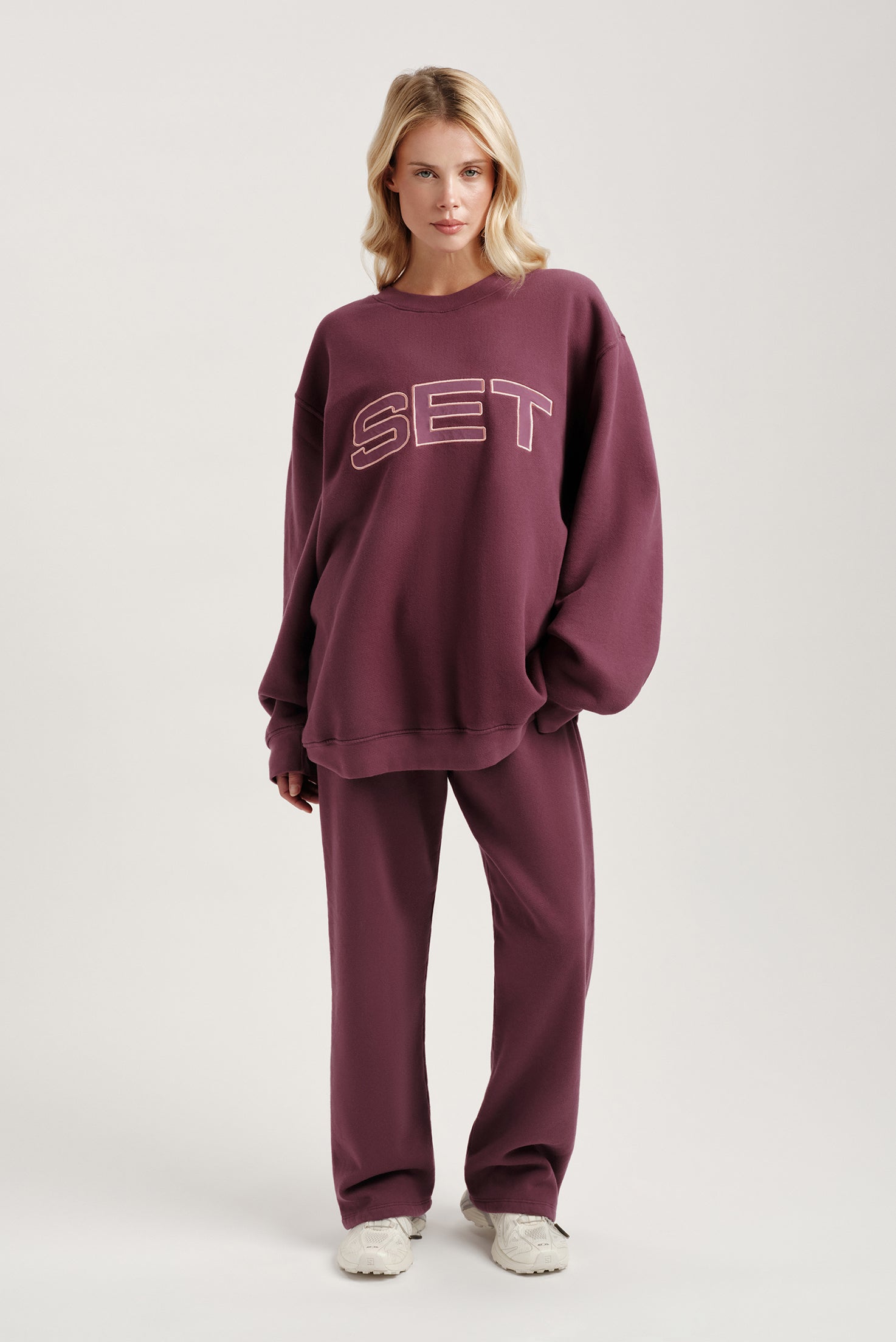 Woman wearing a maroon 'SET' sweatshirt and pants on a white background