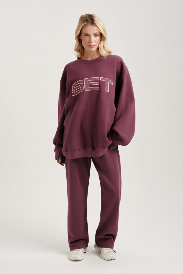 Woman wearing a maroon 'SET' sweatshirt and pants on a light gray background