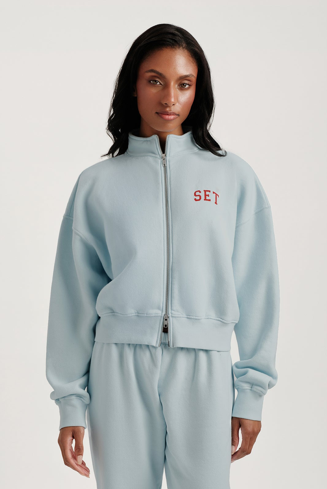 Woman wearing a light blue tracksuit with 'SET' logo on a white background