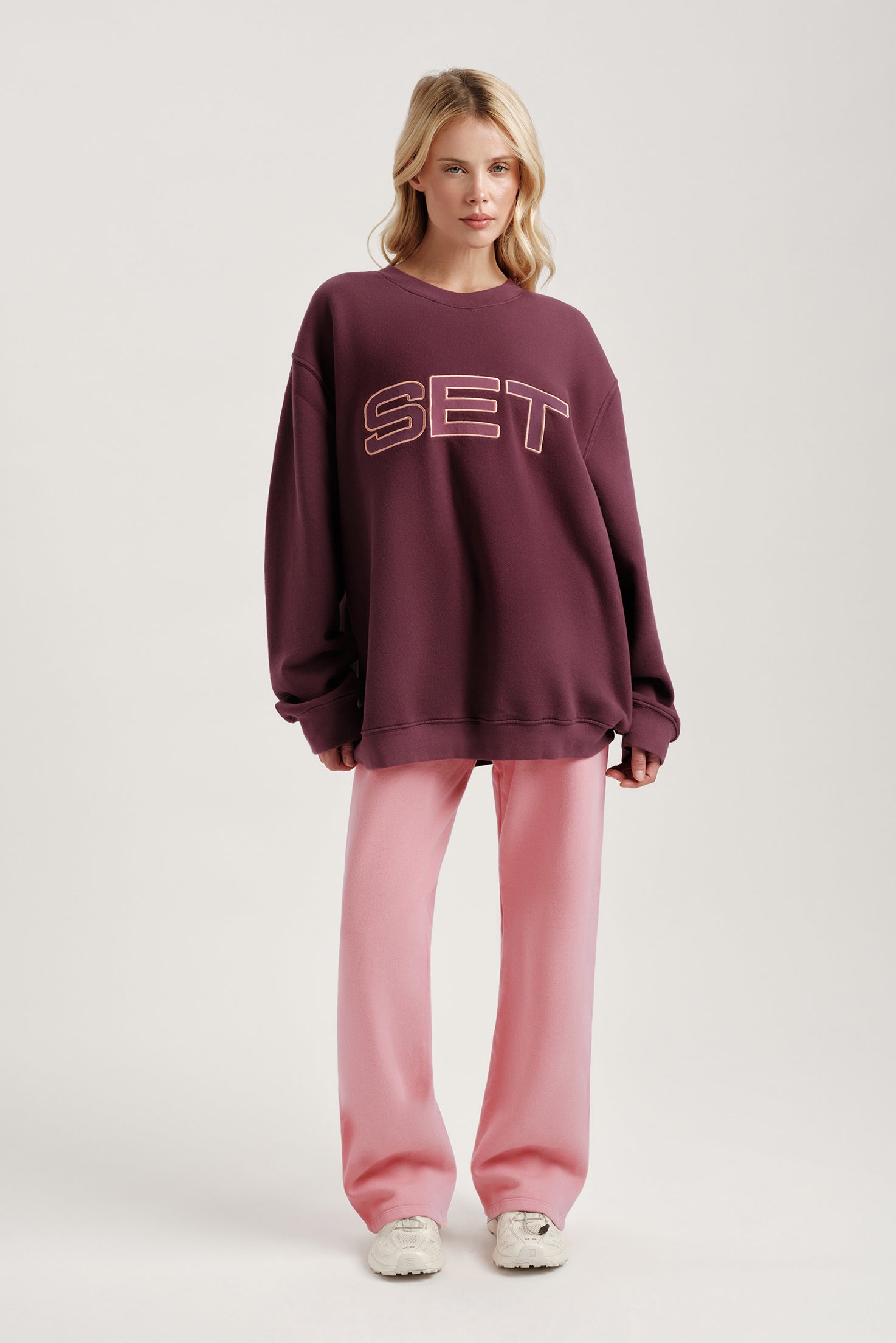 Person wearing a maroon sweatshirt with 'SET' text and pink pants on a light gray background