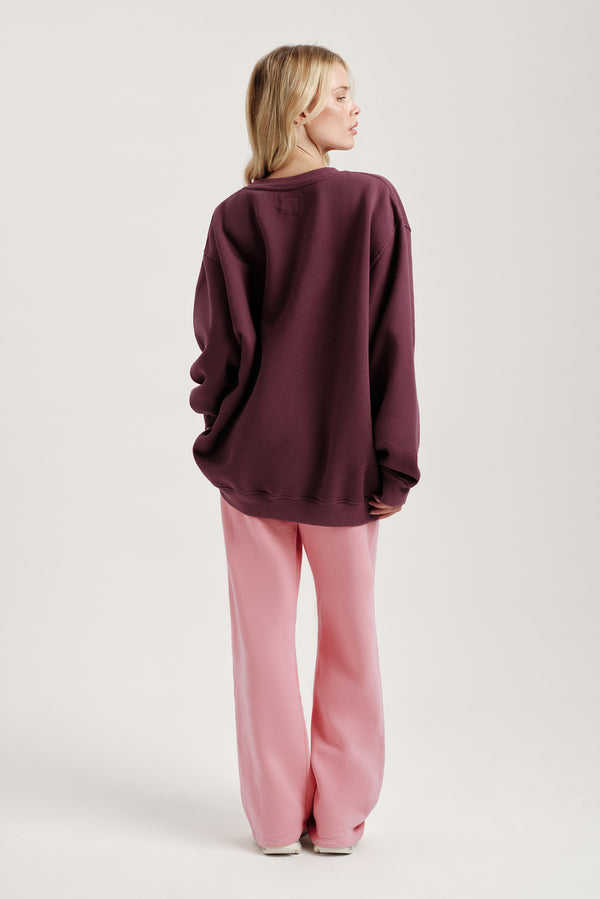 Person wearing a burgundy oversized sweatshirt and pink pants on a light gray background