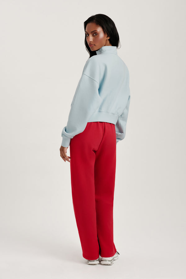 Person wearing a light blue sweatshirt and red pants on a white background