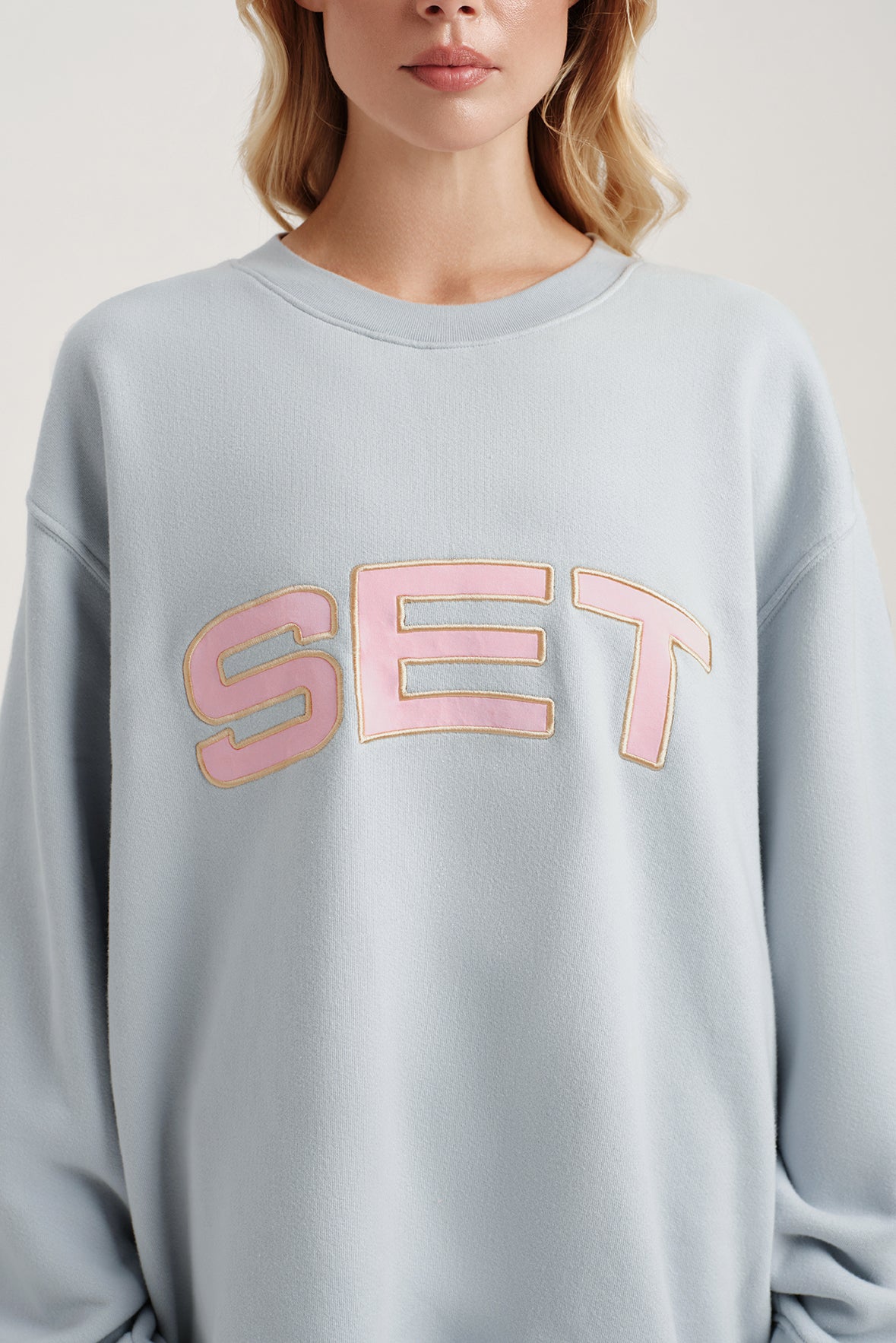 Person wearing a light blue sweatshirt with 'SET' in pink letters.