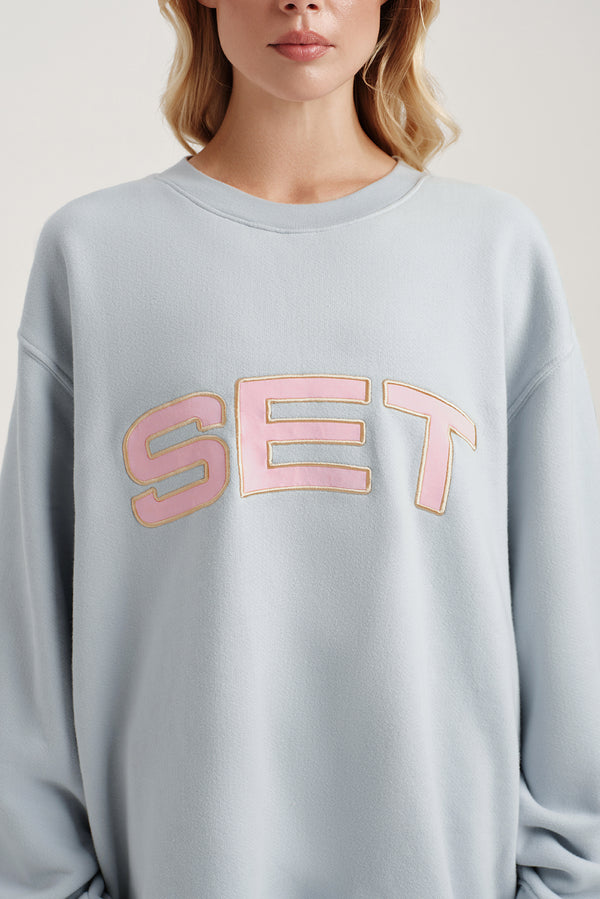 Person wearing a light blue sweatshirt with 'SET' in pink letters.