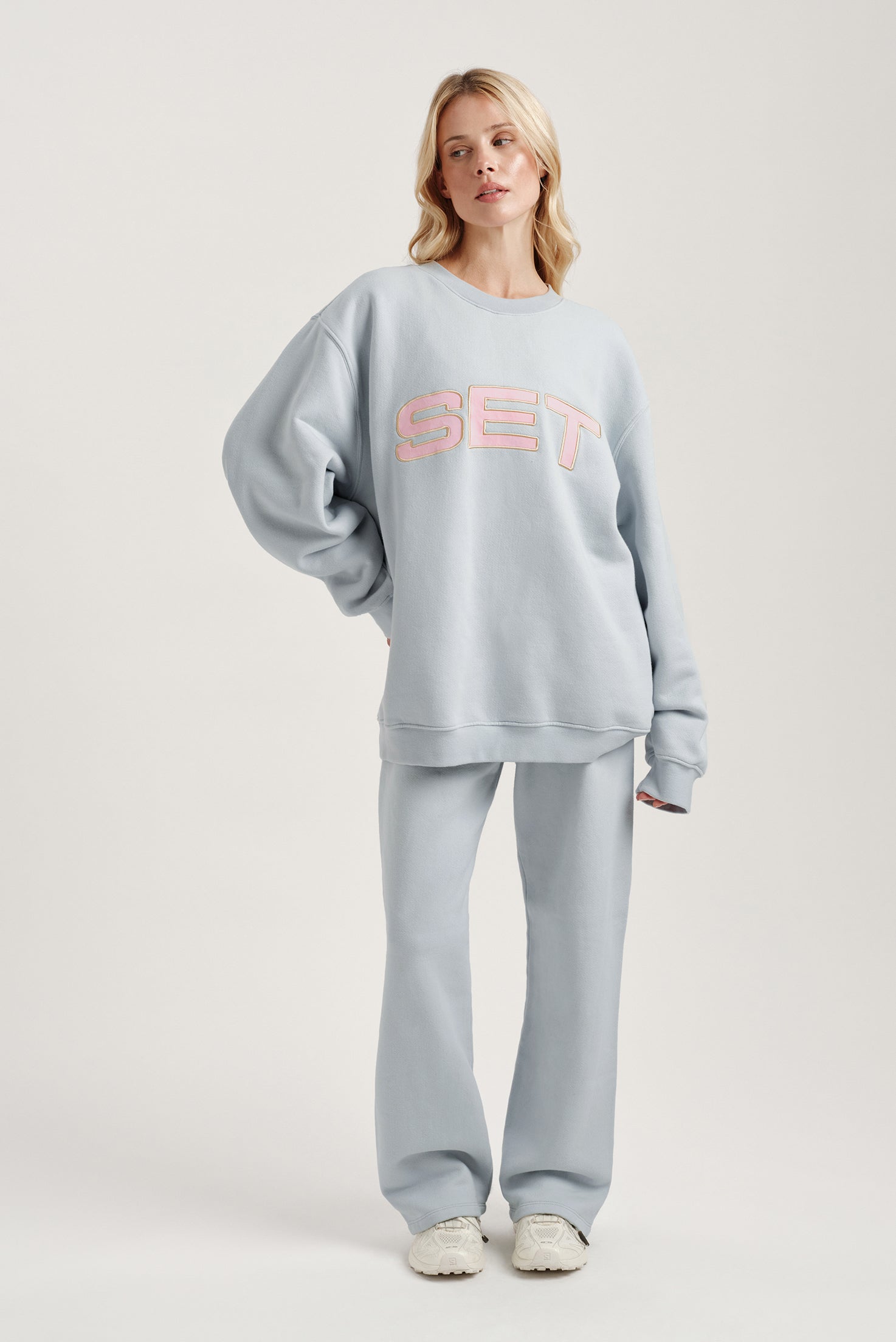 Woman wearing a light gray sweatshirt with 'SET' logo and matching pants on a white background