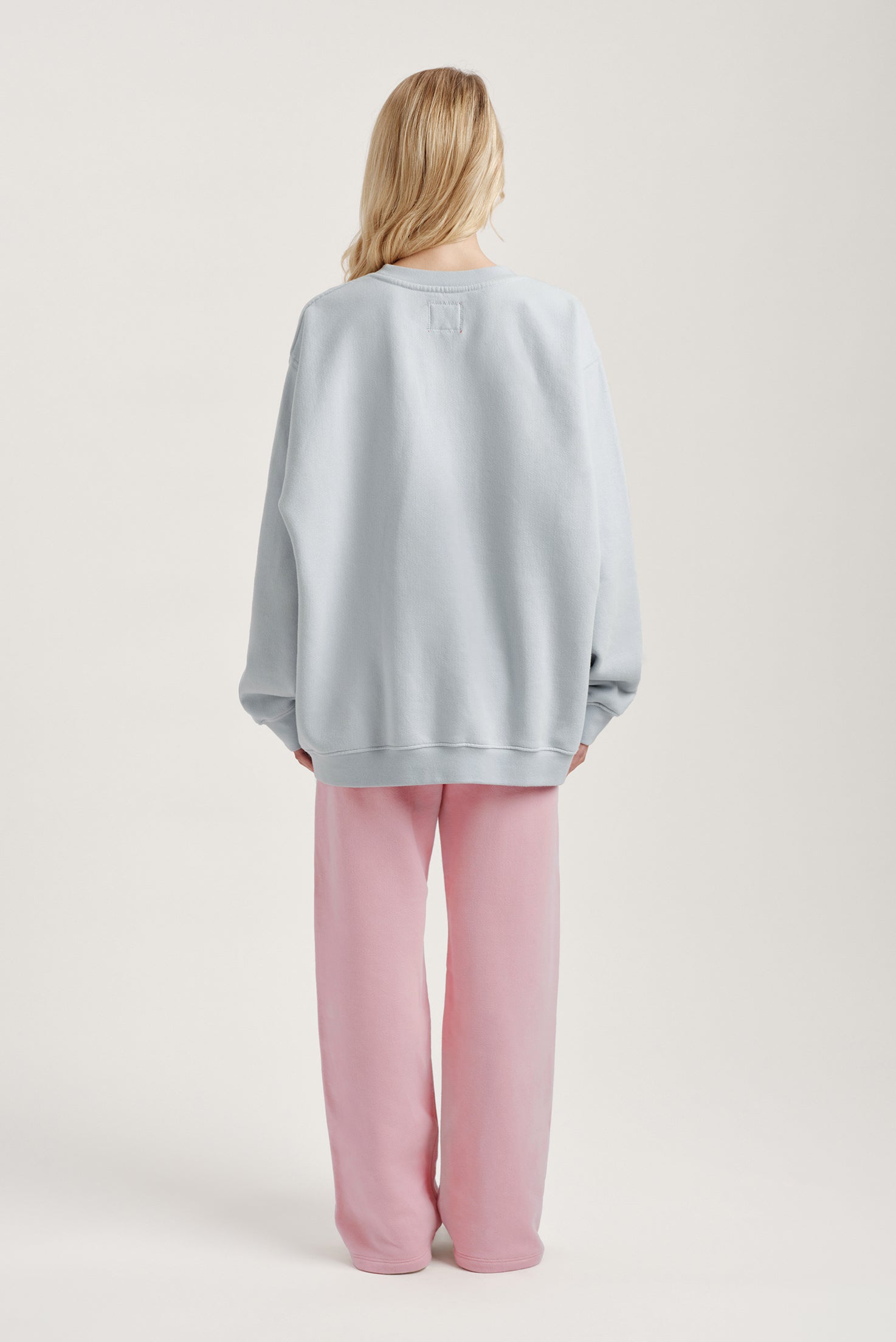 Person wearing a light blue oversized sweater and pink pants on a white background