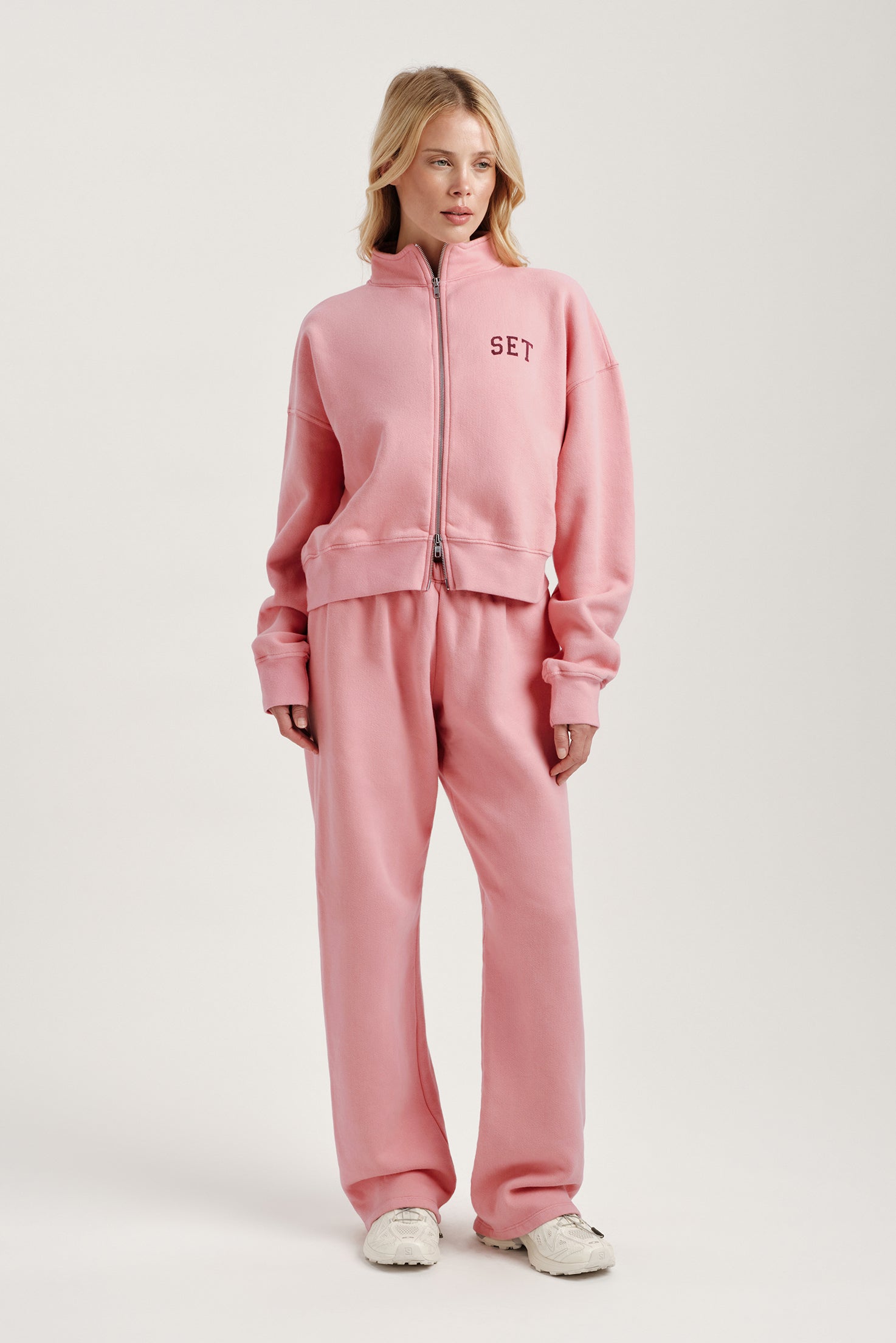 Person wearing a pink tracksuit with 'SET' branding on a white background