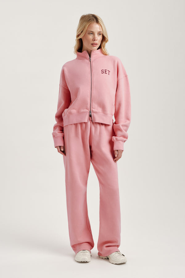Person wearing a pink tracksuit with 'SET' branding on a white background